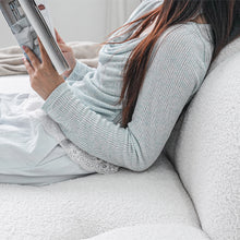 Load image into Gallery viewer, Woman sitting on a couch holding a smartphone with a light blue sweater and white pants.